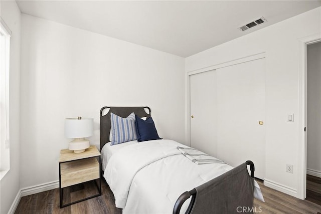 bedroom with wood finished floors, visible vents, a closet, and baseboards