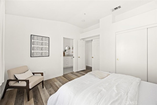 bedroom with wood finished floors, visible vents, baseboards, ensuite bath, and vaulted ceiling