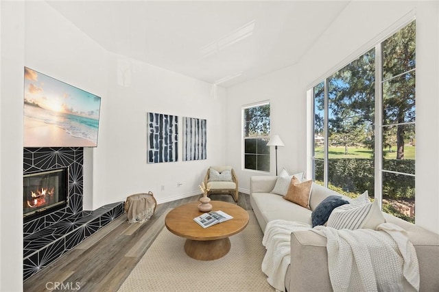 living area featuring a tiled fireplace, baseboards, and wood finished floors