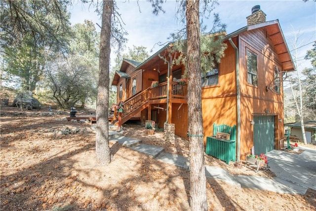 back of property featuring a wooden deck, stairway, an attached garage, and a chimney