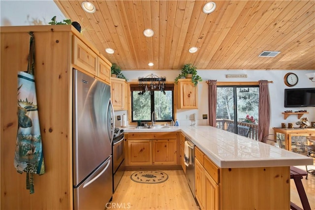 kitchen featuring visible vents, a sink, tile countertops, stainless steel appliances, and a peninsula