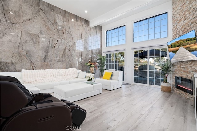 living room with a stone fireplace, recessed lighting, wood finished floors, and a towering ceiling