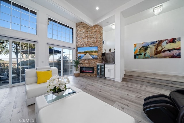 living room with wood finished floors, beverage cooler, baseboards, a high ceiling, and a stone fireplace