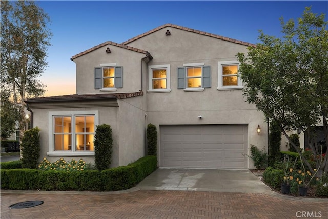 mediterranean / spanish-style house with stucco siding, decorative driveway, and an attached garage