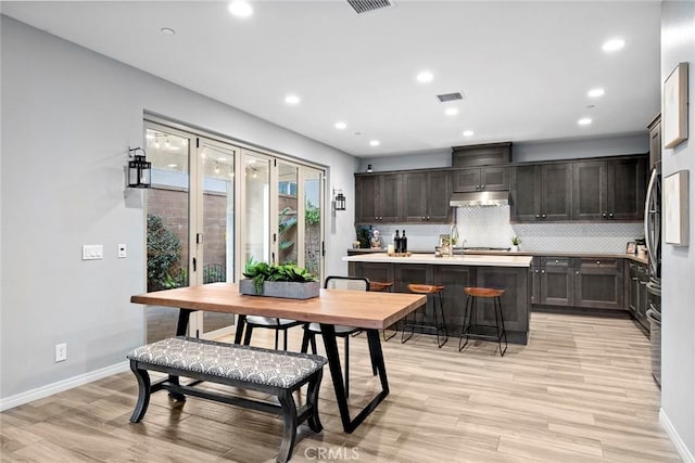 kitchen with backsplash, baseboards, under cabinet range hood, light wood-type flooring, and light countertops