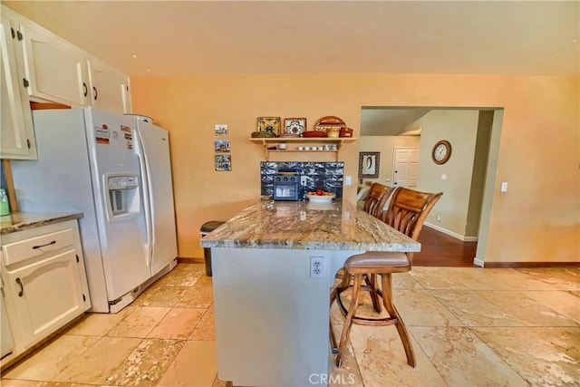 kitchen featuring baseboards, a kitchen breakfast bar, a peninsula, white fridge with ice dispenser, and white cabinetry