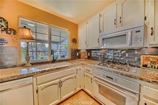 kitchen with white appliances, light stone counters, light tile patterned floors, a sink, and tasteful backsplash