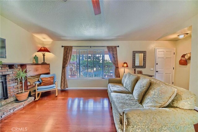 living room featuring a brick fireplace, wood finished floors, baseboards, and a textured ceiling