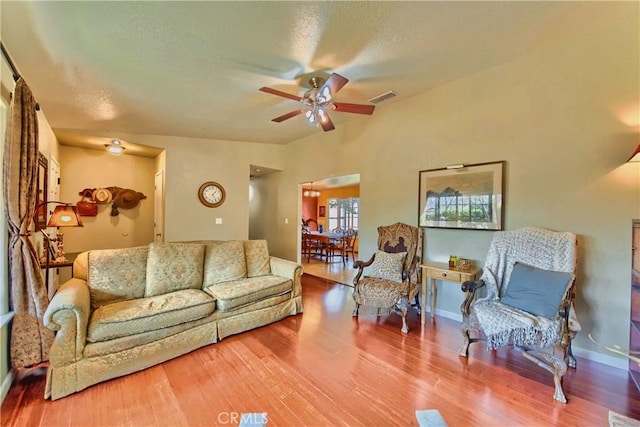 living room featuring visible vents, baseboards, wood finished floors, a textured ceiling, and a ceiling fan