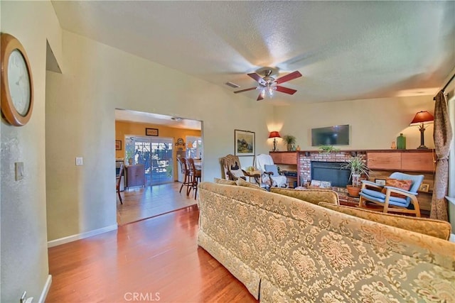 living area featuring visible vents, a textured ceiling, wood finished floors, a fireplace, and baseboards