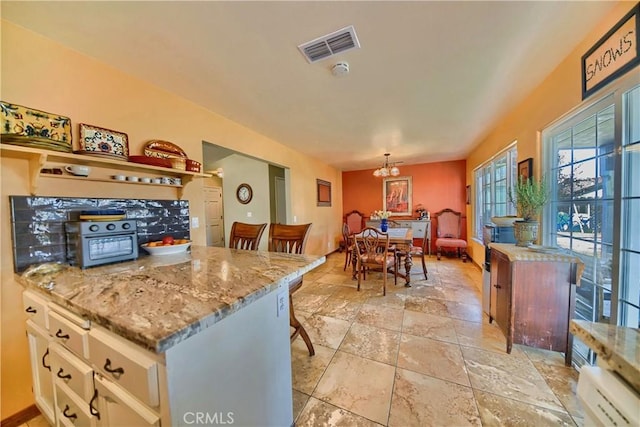 kitchen featuring visible vents, a notable chandelier, pendant lighting, light stone counters, and stone finish flooring