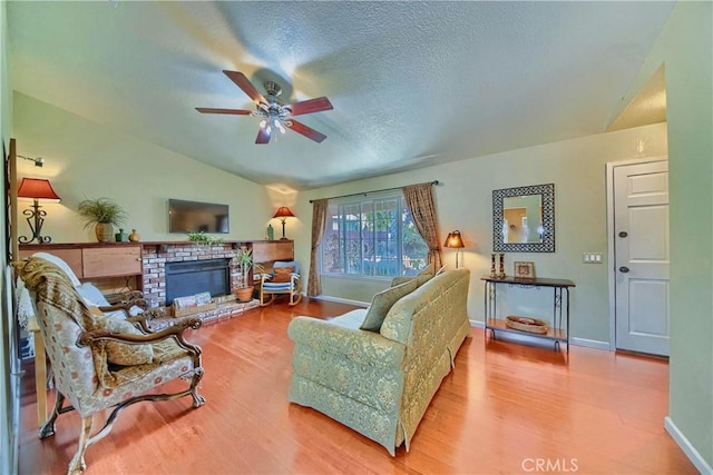 living area featuring a textured ceiling, a brick fireplace, wood finished floors, and vaulted ceiling