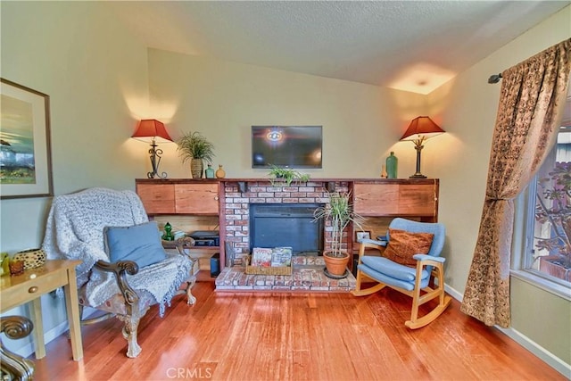 living area with a brick fireplace, a textured ceiling, baseboards, and wood finished floors