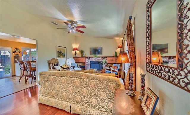 living room with visible vents, a brick fireplace, wood finished floors, a textured ceiling, and a ceiling fan