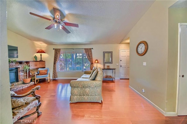 living area with vaulted ceiling, a fireplace, wood finished floors, a textured ceiling, and a ceiling fan