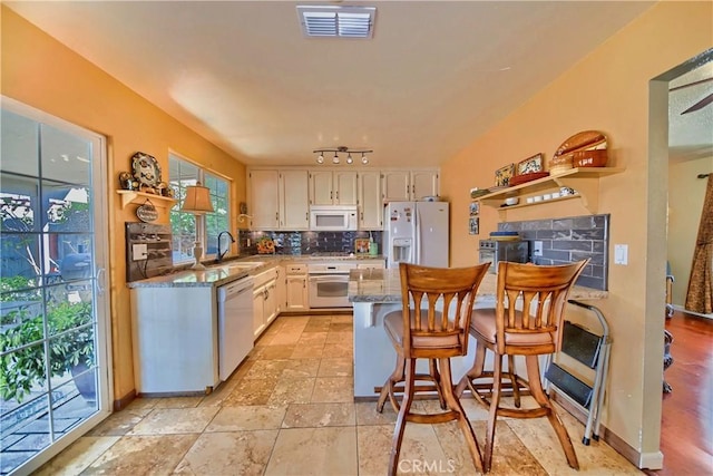 kitchen with a sink, white appliances, a peninsula, white cabinets, and decorative backsplash