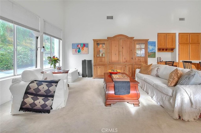 living area featuring carpet flooring, visible vents, and a towering ceiling