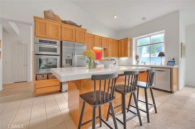 kitchen with a kitchen breakfast bar, a kitchen island, appliances with stainless steel finishes, light tile patterned floors, and tile counters