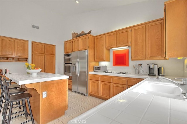 kitchen with a kitchen bar, visible vents, a sink, stainless steel appliances, and tile counters