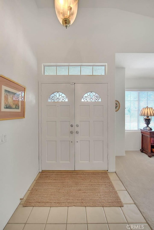 entryway with light tile patterned floors, light colored carpet, and a towering ceiling