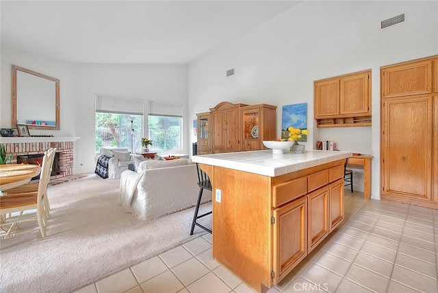 kitchen with visible vents, tile countertops, light carpet, a fireplace, and high vaulted ceiling