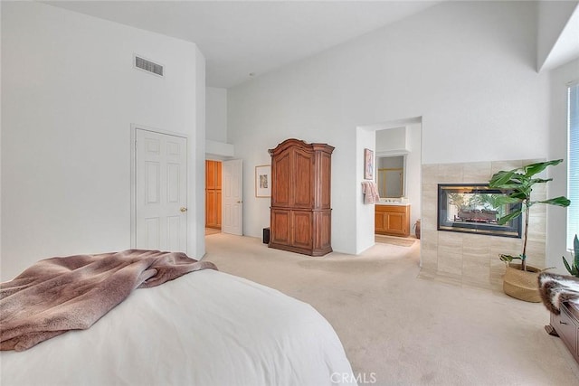 bedroom featuring visible vents, light carpet, a tile fireplace, ensuite bathroom, and high vaulted ceiling