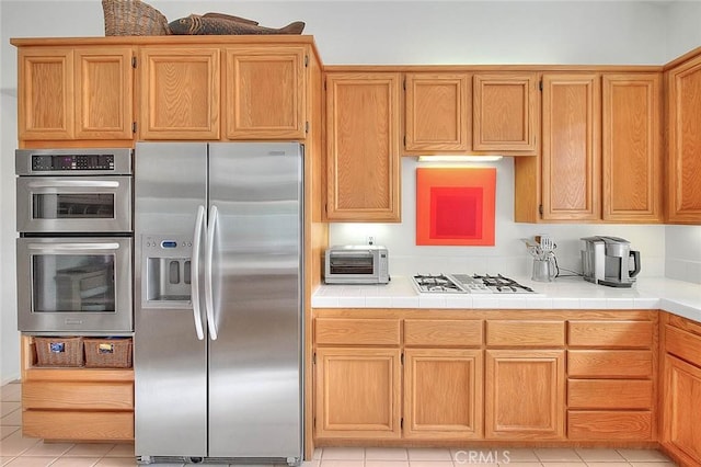 kitchen featuring tile countertops, a toaster, light tile patterned flooring, and appliances with stainless steel finishes