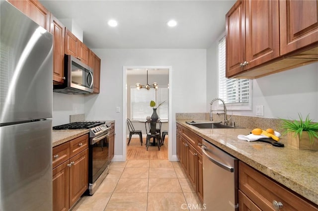 kitchen with a chandelier, brown cabinets, appliances with stainless steel finishes, light tile patterned flooring, and a sink