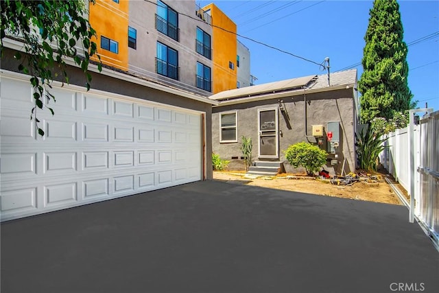 view of front of home with stucco siding, solar panels, driveway, and fence