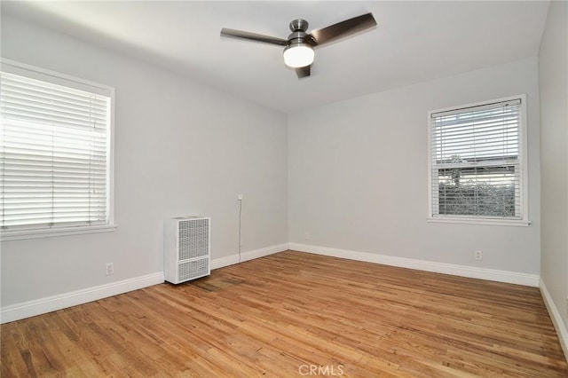 empty room with heating unit, a ceiling fan, light wood-style floors, and baseboards
