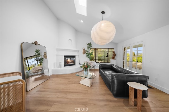 living area featuring wood finished floors, baseboards, a skylight, french doors, and a large fireplace