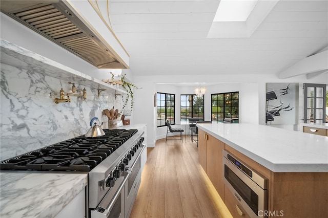 kitchen featuring a wealth of natural light, lofted ceiling with skylight, stainless steel appliances, exhaust hood, and light wood finished floors