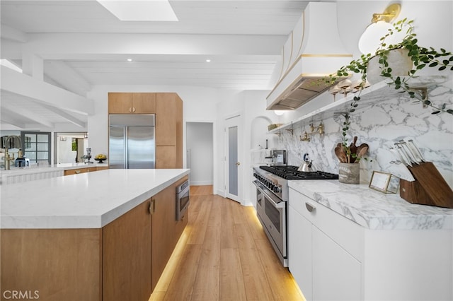 kitchen with premium range hood, light wood-type flooring, a kitchen island, decorative backsplash, and built in appliances