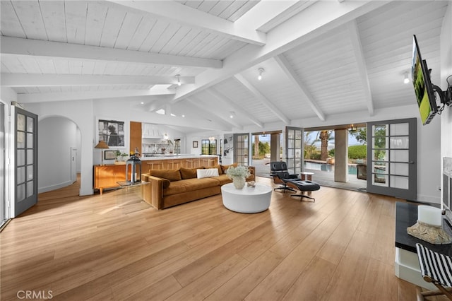 living room with plenty of natural light, french doors, arched walkways, and vaulted ceiling with beams