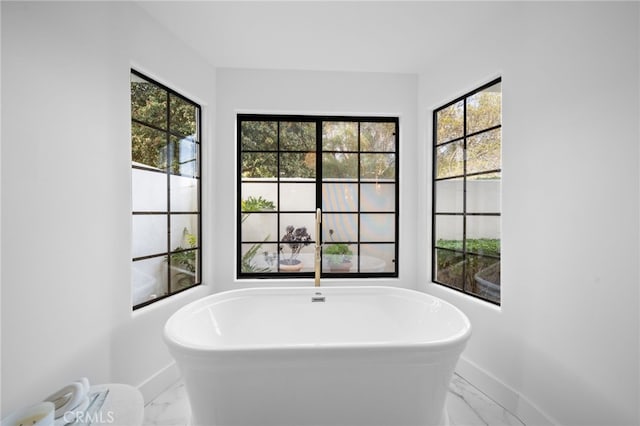 bathroom with marble finish floor, a freestanding bath, and baseboards