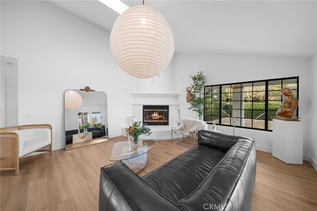 living room with high vaulted ceiling, a large fireplace, baseboards, and wood finished floors