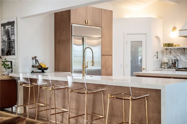 kitchen featuring a kitchen bar, tasteful backsplash, built in fridge, a peninsula, and light countertops