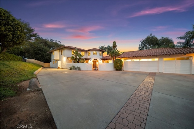 mediterranean / spanish home featuring a tiled roof, stucco siding, driveway, and fence