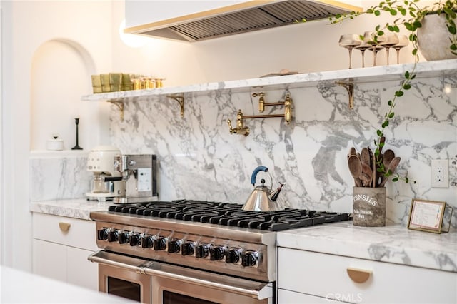 kitchen featuring light stone countertops, double oven range, custom exhaust hood, white cabinets, and backsplash