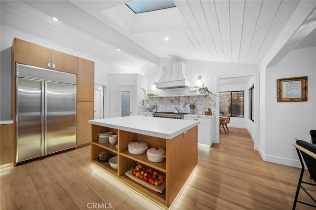 kitchen with vaulted ceiling with beams, built in refrigerator, light countertops, custom exhaust hood, and open shelves