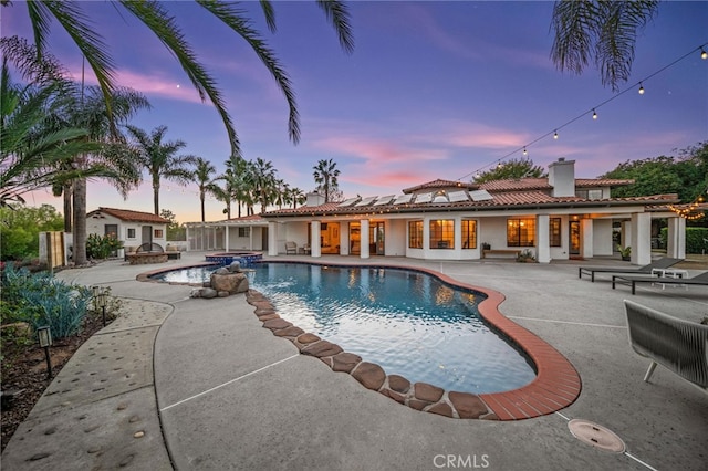 pool at dusk featuring a patio and a pool with connected hot tub