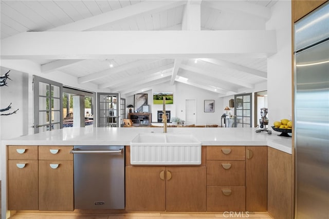 kitchen featuring vaulted ceiling with beams, light countertops, appliances with stainless steel finishes, brown cabinetry, and a sink