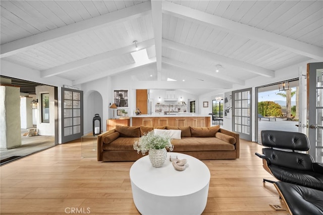 living area featuring french doors, arched walkways, vaulted ceiling with beams, and light wood finished floors