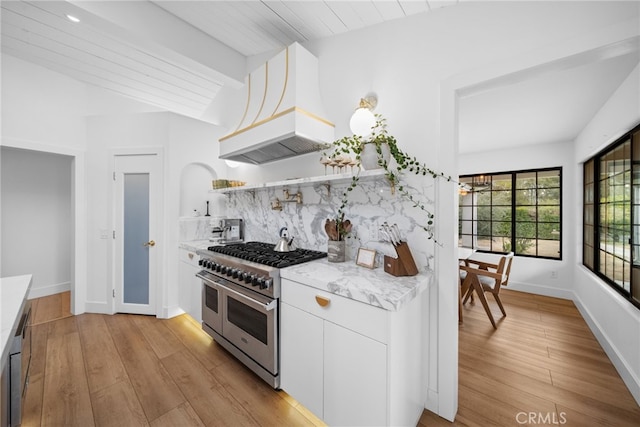 kitchen with light wood-type flooring, lofted ceiling with beams, double oven range, tasteful backsplash, and white cabinetry