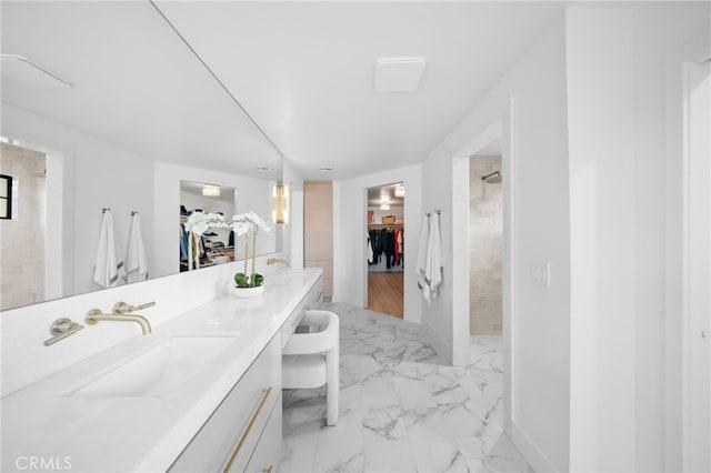 full bath featuring marble finish floor, tiled shower, a walk in closet, and a sink