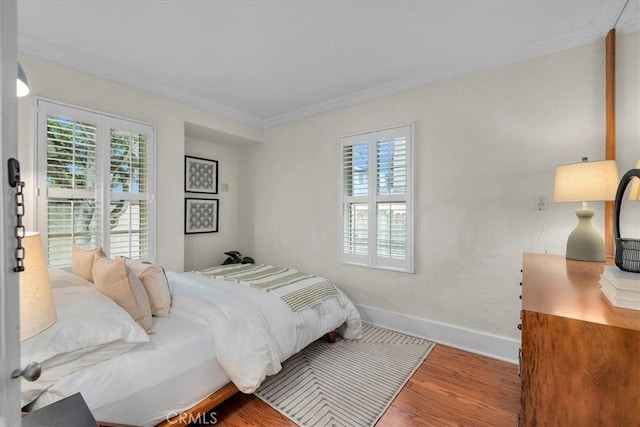 bedroom with multiple windows, crown molding, baseboards, and wood finished floors