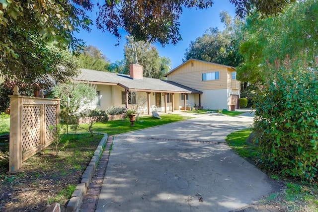 view of front facade with a chimney, concrete driveway, and a front yard