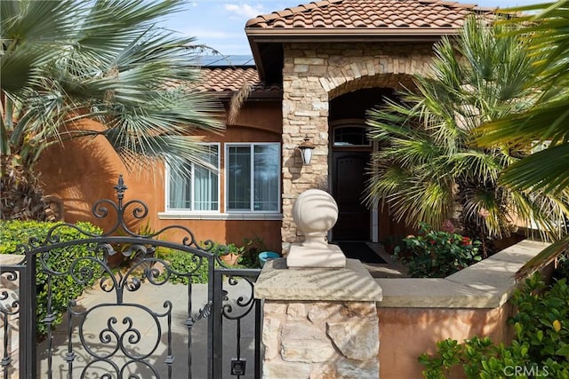 entrance to property featuring solar panels, fence, a tiled roof, stone siding, and a gate