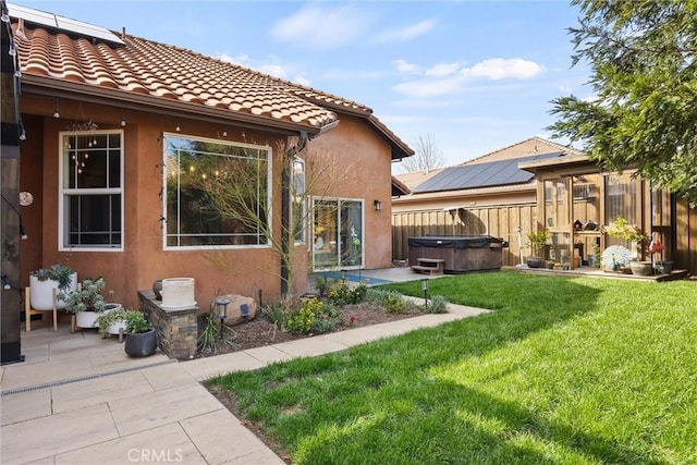 rear view of property with a hot tub, fence, stucco siding, a yard, and a patio