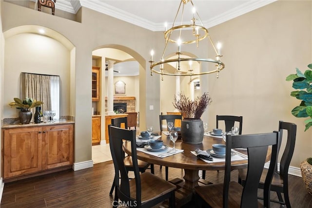 dining area with a stone fireplace, crown molding, dark wood-style floors, and arched walkways